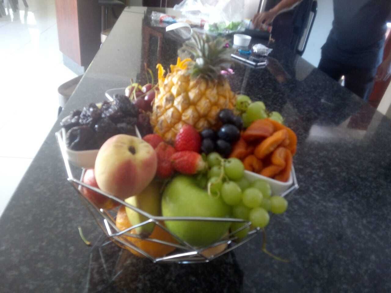 A fruit basket on a kitchen counter with various fruits including apples, grapes, and a pineapple.