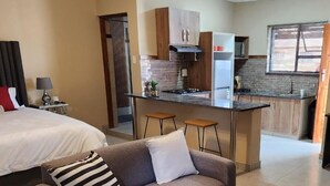 A modern hotel room with a sofa, a small table, a bed, a kitchenette, and a bathroom visible through a door. - Hush Guest House (Thabazimbi)