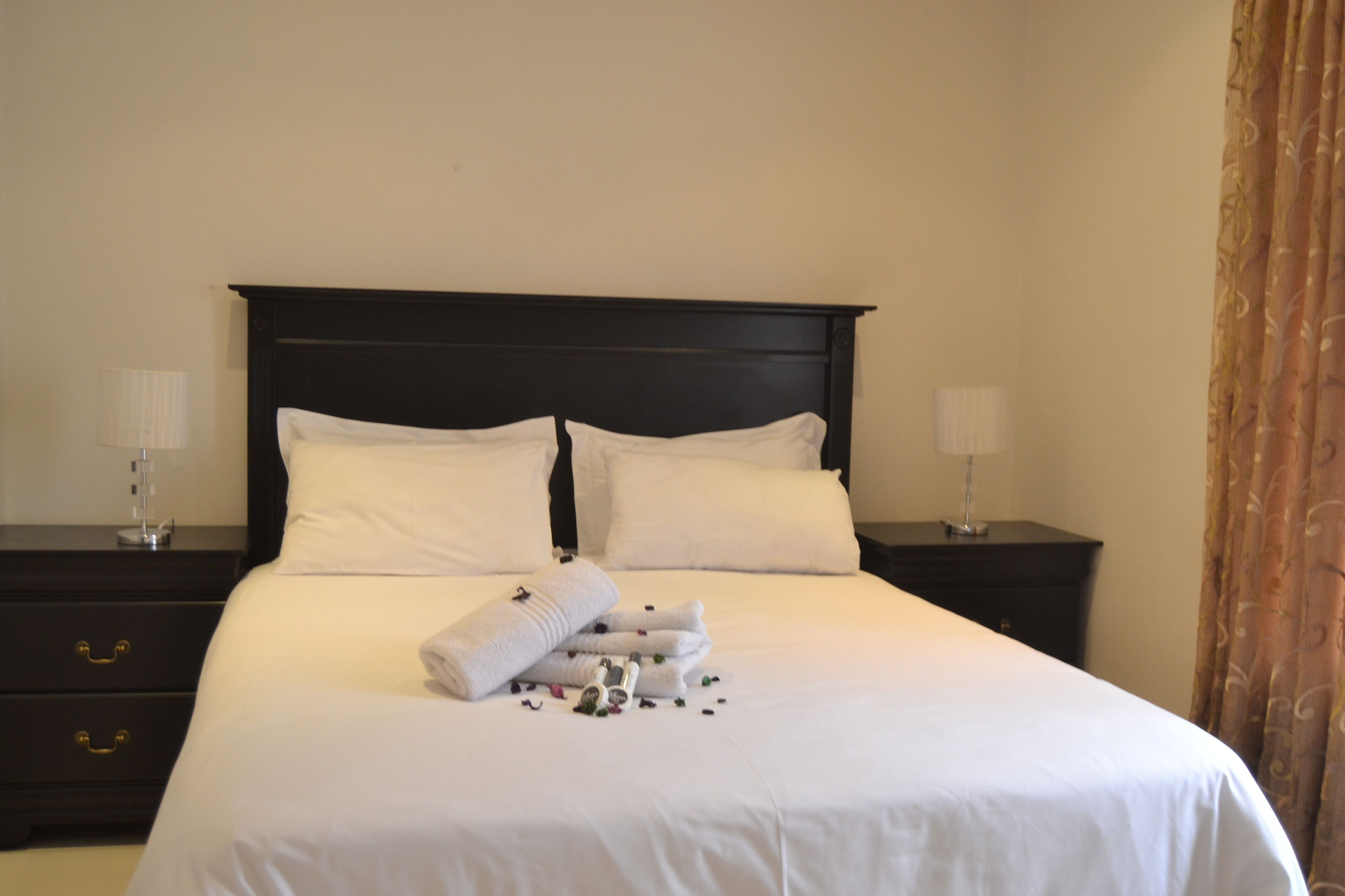 A neatly made bed with white linens, two bedside tables with lamps, and a dark headboard.