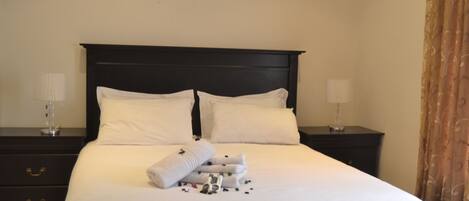 A neatly made bed with white linens, two bedside tables with lamps, and a dark headboard.