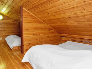 Una habitación tipo cabaña de madera con una cama individual, un ventanal pequeño y un techo inclinado.