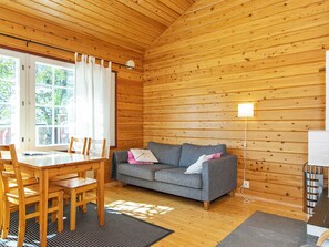 L’intérieur d’un chalet accueillant, avec un décor en bois, une table à manger entourée de chaises, un canapé et une fenêtre agrémentée de rideaux.