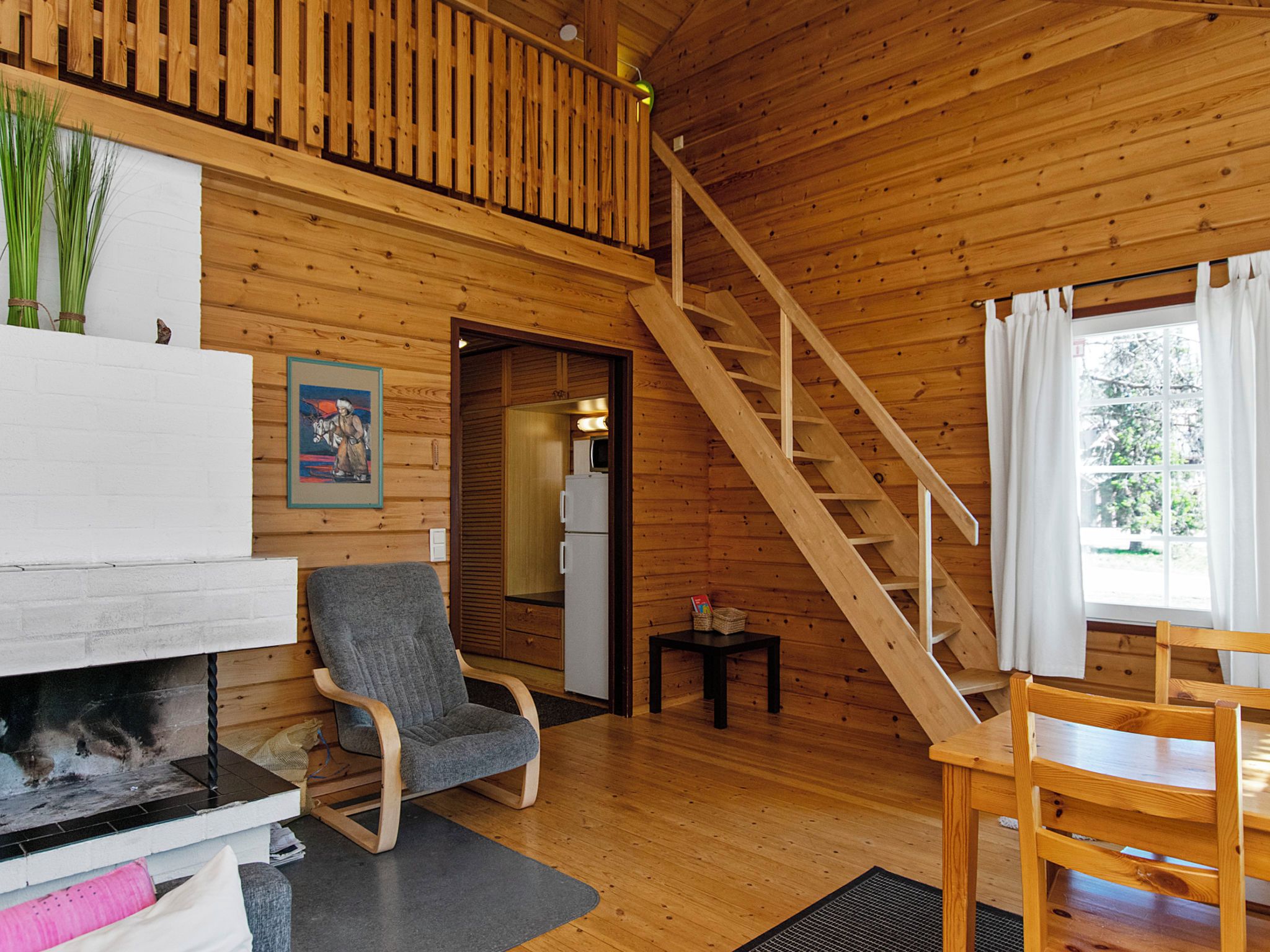 A wooden cabin interior with a fireplace, a dining area, a staircase, and a view of the outdoors.