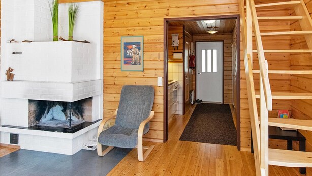 Interior acogedor de una cabaña con chimenea, una escalera de madera y un cuadro en la pared.