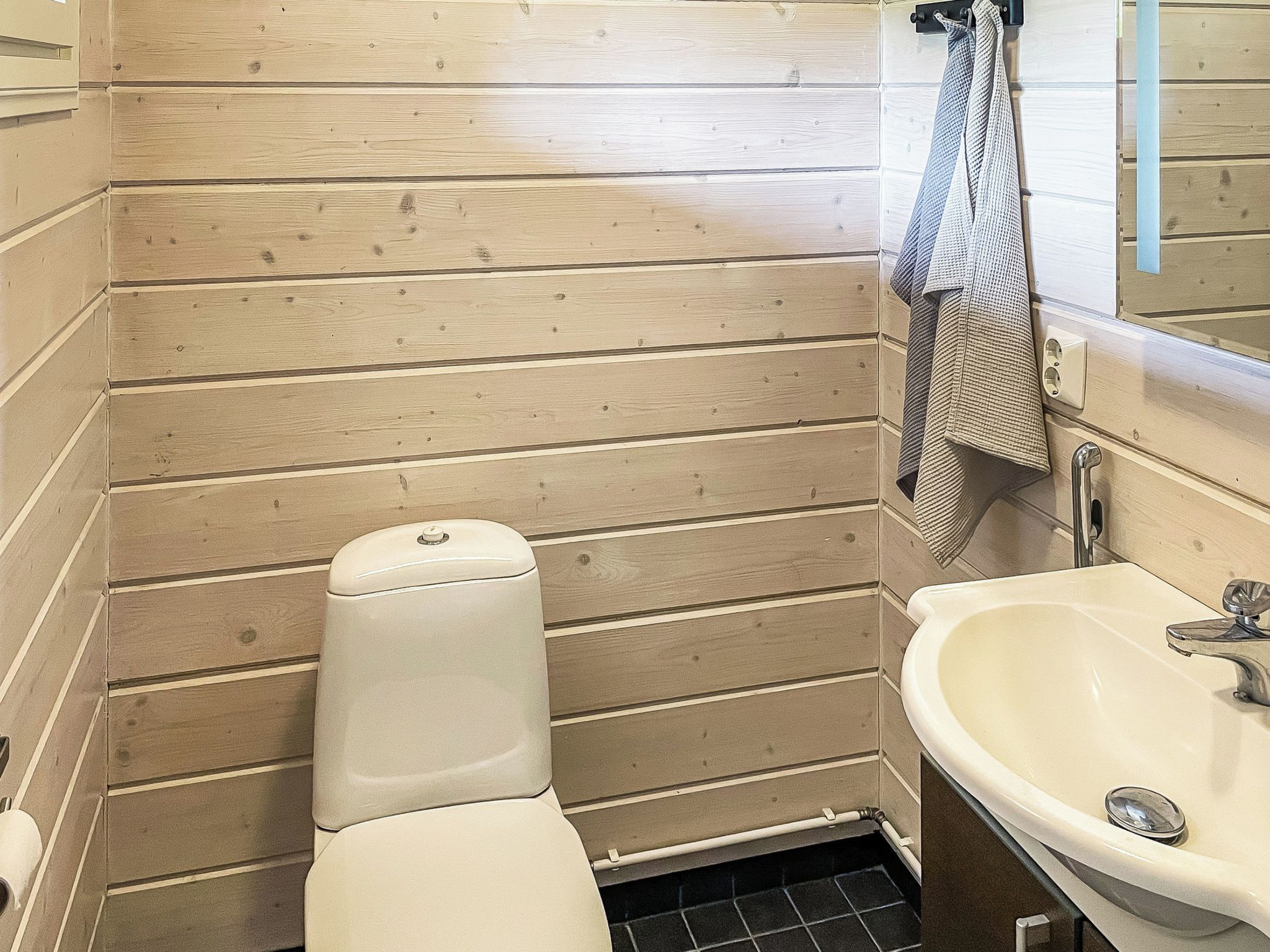 A compact bathroom with a toilet, sink, and wooden panel walls.