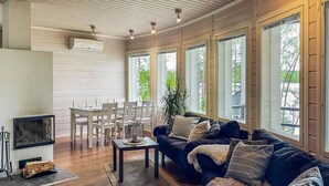 Ein geräumiges Wohnzimmer mit einem dunkelgrauen Sofa, einem Couchtisch und einem Kamin. Mehrere Fenster sorgen für natürliches Licht und Blick ins Grüne.