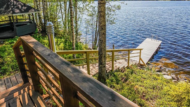 Eine Holzterrasse mit einer Bank mit Blick auf einen See, umgeben von Bäumen.
