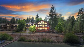 A lodge with a large central building featuring a prominent balcony, surrounded by dense forest and a calm lake. - Lakeview Lodge By Destination Big Bear: Lakefront Luxury with Dock & Views! Hot Tub! Near Village! (Big Bear Lake)
