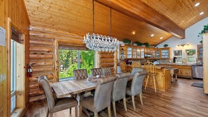 A log cabin interior with a dining area, kitchen, and large windows.