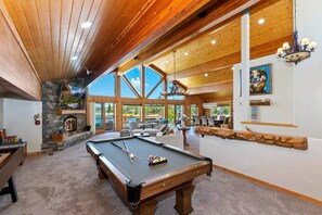 A pool table in a room with wooden beams, a stone fireplace, and a view of the outdoors.