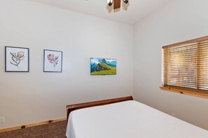 A bedroom with a bed, a window with blinds, and three framed pictures on the wall. - Lakeview Lodge By Destination Big Bear: Lakefront Luxury with Dock & Views! Hot Tub! Near Village! (Big Bear Lake)
