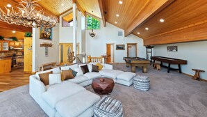 A spacious living area with a sectional sofa, a pool table, and a wooden ceiling.