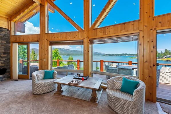 A spacious room with large windows, a wooden ceiling, and a view of a lake.
