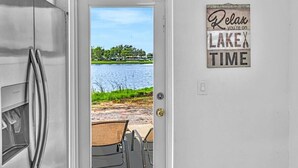 Una cocina con un refrigerador de acero inoxidable, una puerta que da a vista del lago, y un letrero que dice 'Relájate, estás de VACACIONES EN EL LAGO'.