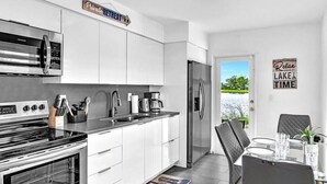 Una cocina moderna con armarios blancos, un refrigerador de acero inoxidable y un comedor con mesa y sillas.