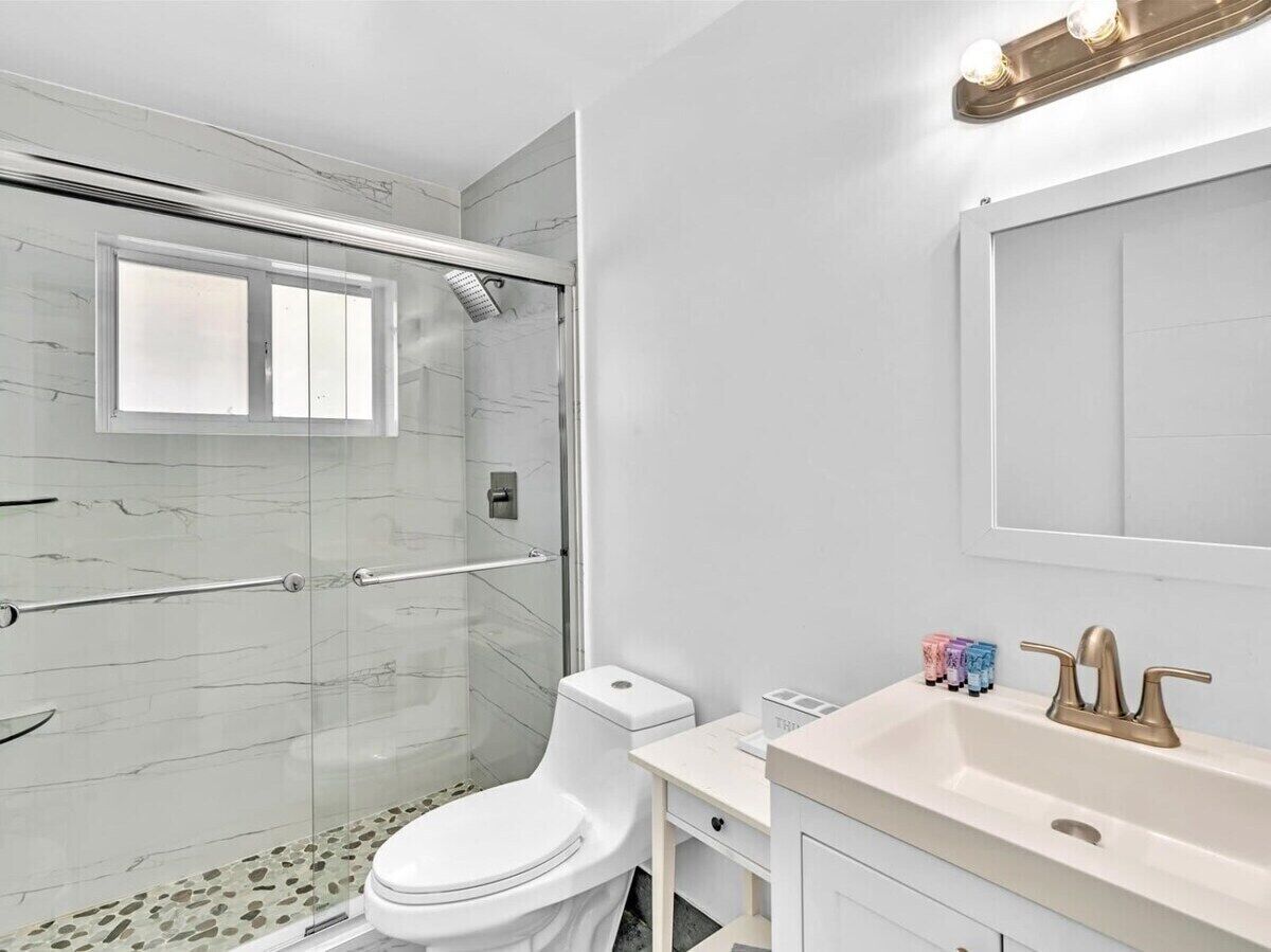 A modern bathroom with a shower, toilet, vanity, and a large mirror.