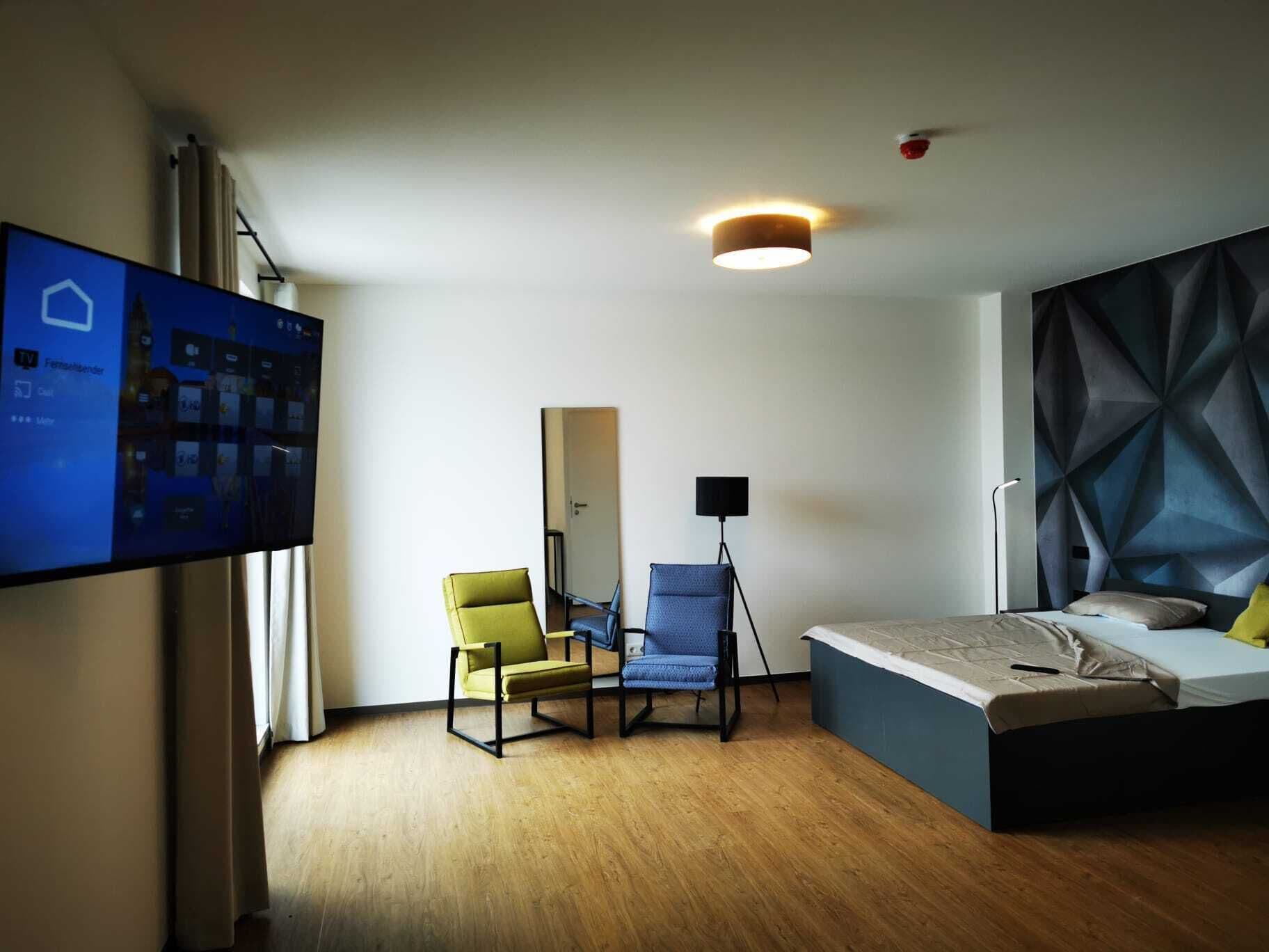 Een moderne hotelkamer met een bed, twee stoelen, een bureau, een flatscreen-tv en een hoofdeinde met een geometrisch patroon.