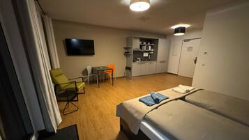A hotel room with a bed, a desk, a chair, a television, and a kitchenette.