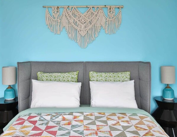 A bed with a geometric-patterned quilt, two pillows, and a macramé wall hanging. - Lakeside PEC: Beautiful Waterfront & Patio (Wellington)