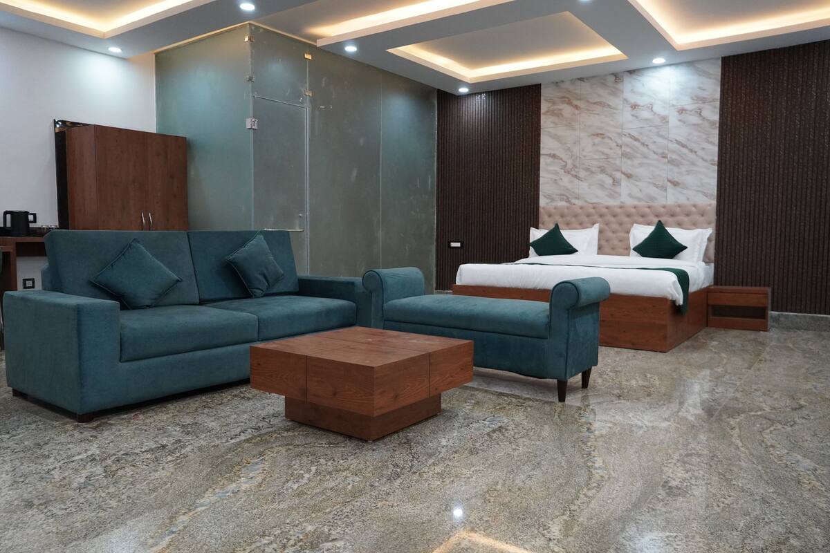 A modern hotel room with a sofa set, a wooden coffee table, a bed with green pillows, and a marble floor.