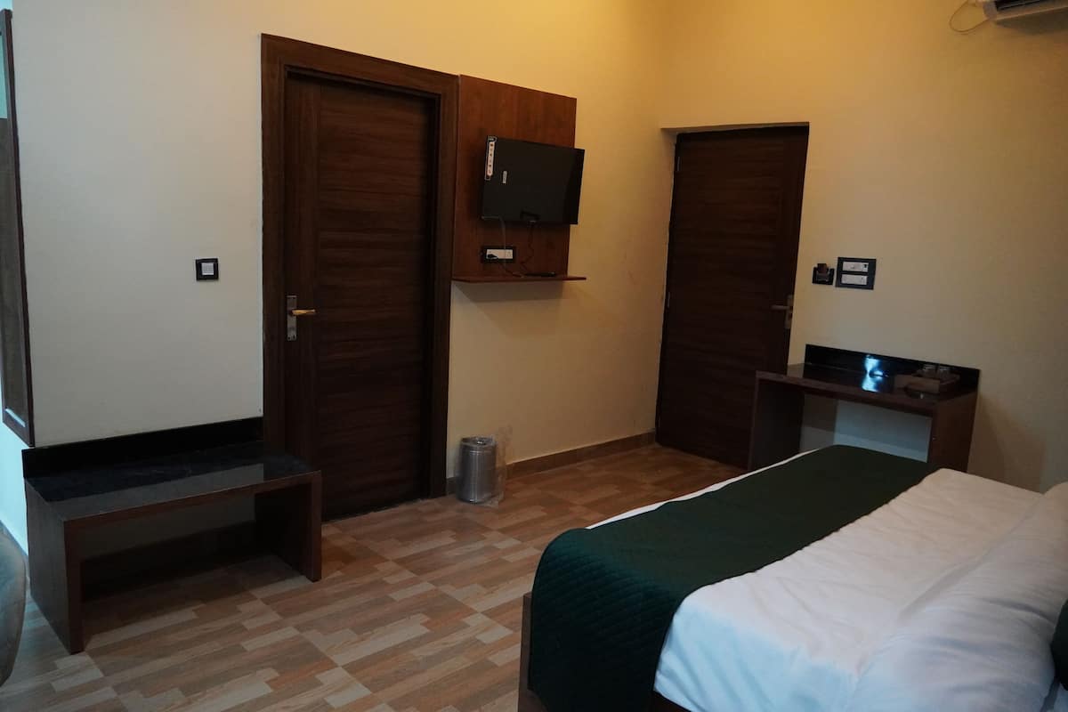 A bedroom with a bed, a wooden bench, a TV mounted on the wall, and a trash bin.