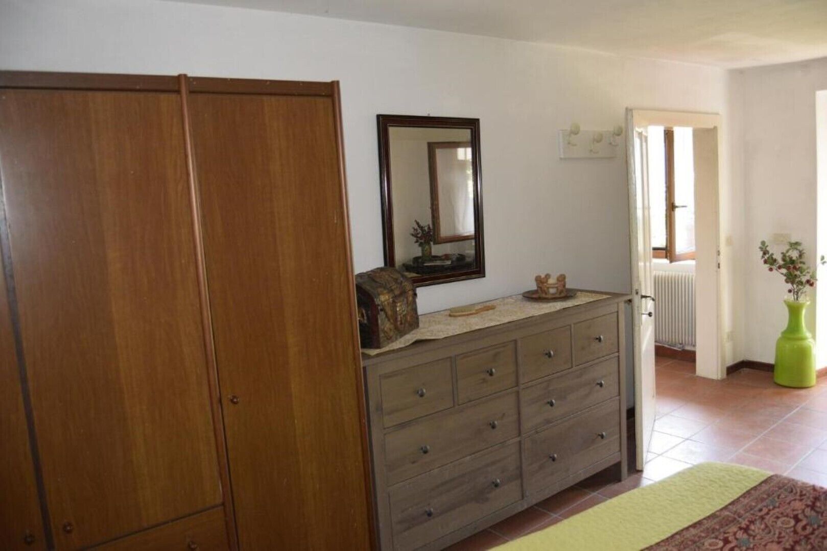 Une pièce comprenant une armoire en bois, une commode avec des tiroirs, un miroir et un radiateur.