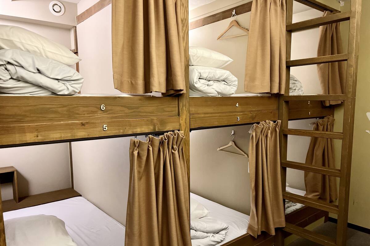A bunk bed room with wooden frames, numbered beds, and beige curtains.