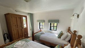 A bedroom with two beds, wooden headboards, and a large wooden wardrobe. - Shipload Cottage (Bideford)