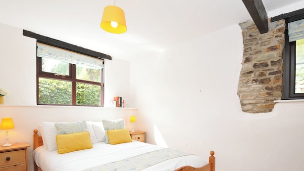 Een slaapkamer met een houten bed, twee nachtkastjes met lampen, een raam met uitzicht op groen, en een stenen muur.