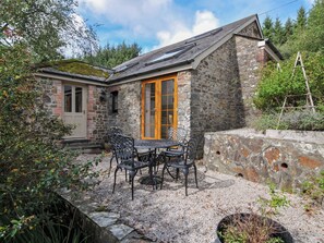 A stone cottage with a wooden door, a gravel patio, and outdoor furniture. - Shipload Cottage (Bideford)
