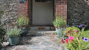 Een stenen cottage met een witte deur, bloempotten en een stenen pad.