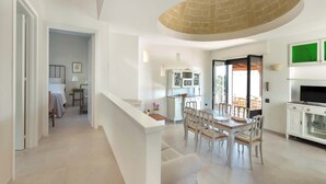 A spacious living area with a dining table, white furniture, a kitchen area, and a TV. - VILLA TWO SORDS, with swimming pool, olive grove, orchard, tropical garden! (Ugento)