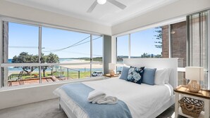 Un dormitorio con una cama grande, vista a la playa y un balcón con barandilla.