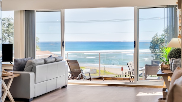 Una sala de estar moderna con un amplio ventanal corredera que da a un balcón con vistas al océano.