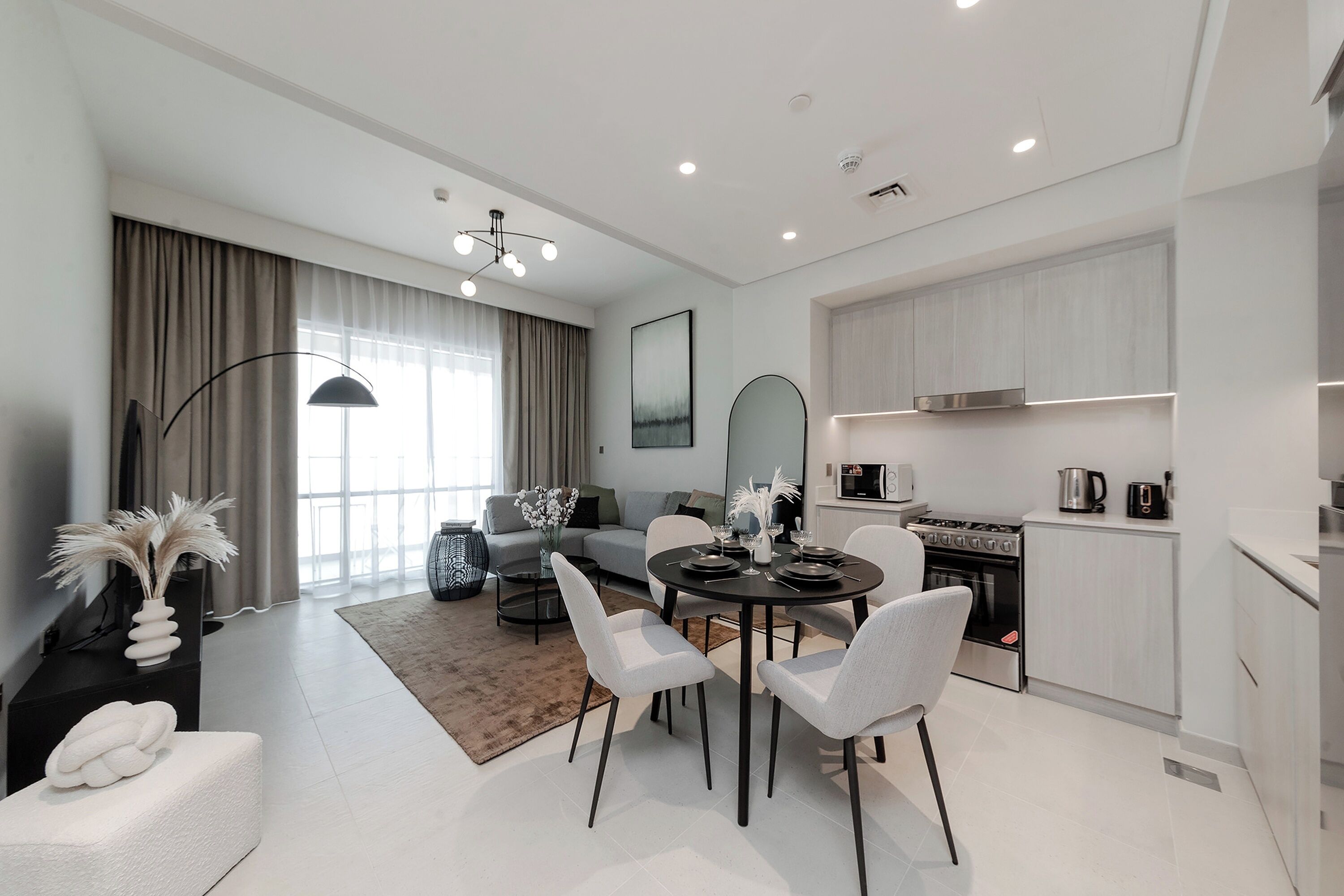 A modern living room with a dining table, chairs, a sofa, and a kitchen area with cabinets and appliances.
