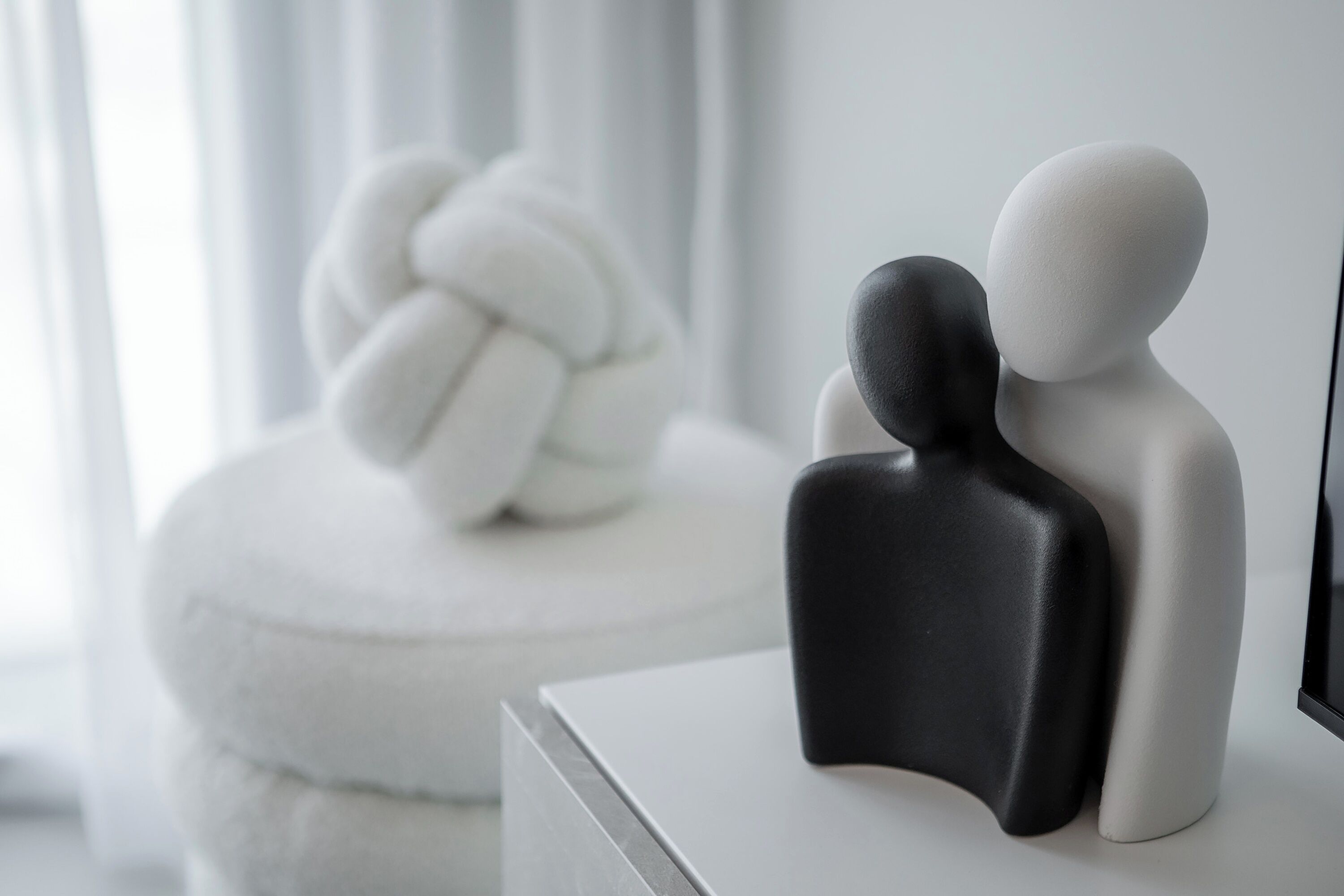 Una habitación minimalista con un sofá blanco y una escultura de nudo decorativo en blanco.
