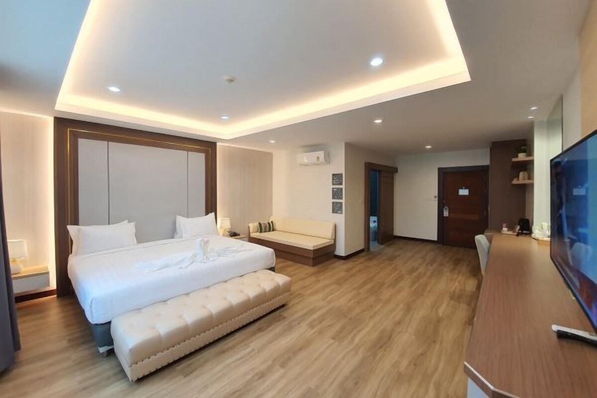 A modern hotel room with a large bed, a sofa, a TV, and a wooden floor.