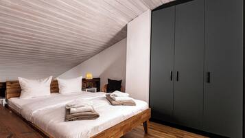 Ein Schlafzimmer mit schrägem Dach, einem hölzernen Bett, einem dunklen Kleiderschrank und einem Nachttisch mit Lampe.