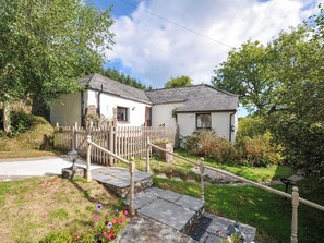 A two-story house with a stone staircase leading to the front door, surrounded by a wooden fence and a garden with flowers.