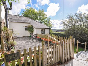 A cottage with a gravel driveway, wooden fence, and a sign indicating its name.