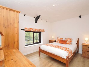 A bedroom with a wooden bed, a window with a view, a bedside table, and a nightstand.