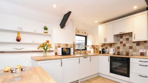 A modern kitchen with white cabinets, a wooden countertop, a microwave, a sink, and an oven. - Windbury Cottage (Bideford)