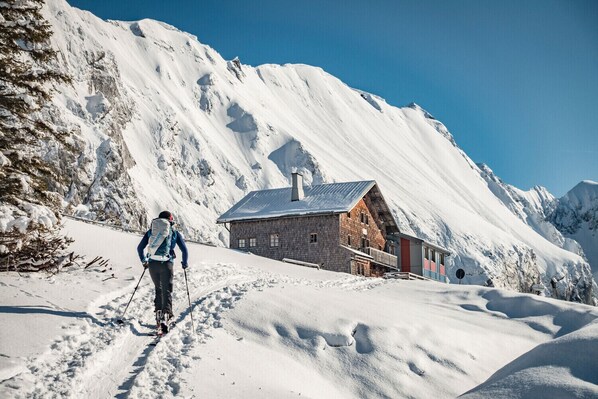 A snow-covered mountain with a wooden cabin and a person skiing.