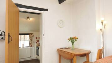 A room with a wooden door, a table with a vase of flowers, a clock on the wall, and a radiator.