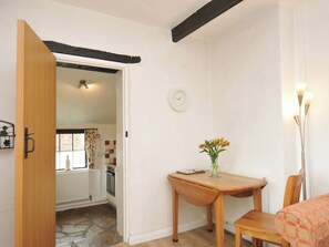 A room with a wooden door, a table with a vase of flowers, a clock on the wall, and a radiator. - Barley Cottage (Bideford)
