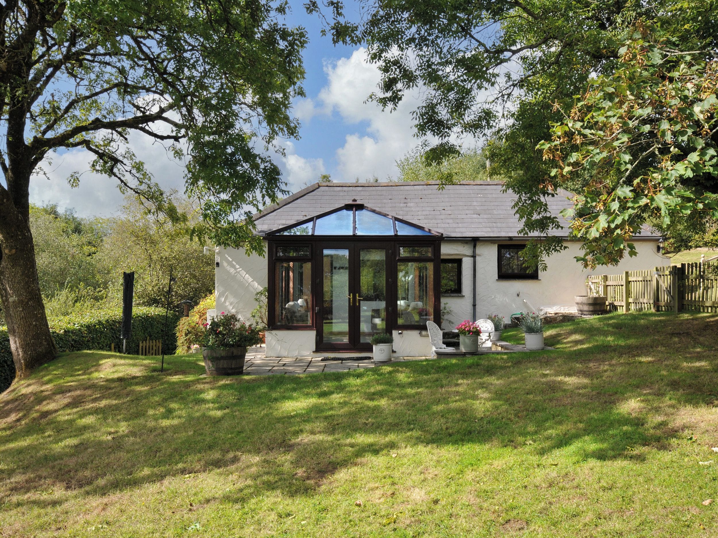 A house with a conservatory, a lawn, and a wooden fence.