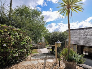 A garden pathway leading to a building with a stone roof, surrounded by lush greenery and a wooden fence. - Barley Cottage (Bideford)