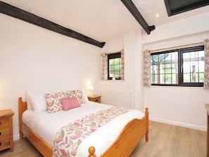 A bedroom with a wooden bed, a nightstand, a window with curtains, and a radiator. - Barley Cottage (Bideford)