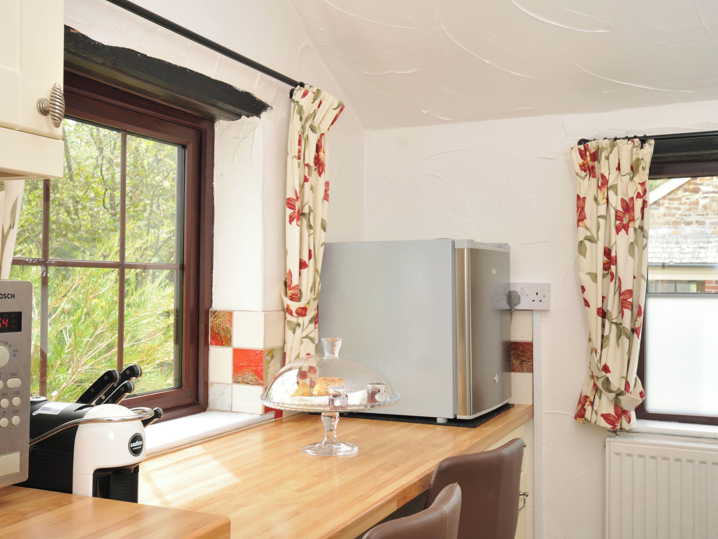 A kitchen with a Bosch appliance, a refrigerator, and a window with floral curtains.