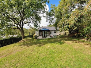 A house with a conservatory, surrounded by a well-maintained lawn and mature trees.